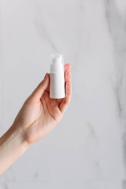 A white bottle with cream in its hand on a white marble background. The isolated object. Bank without stickers. DIY-cosmetics in the bathroom. - Foto, immagini