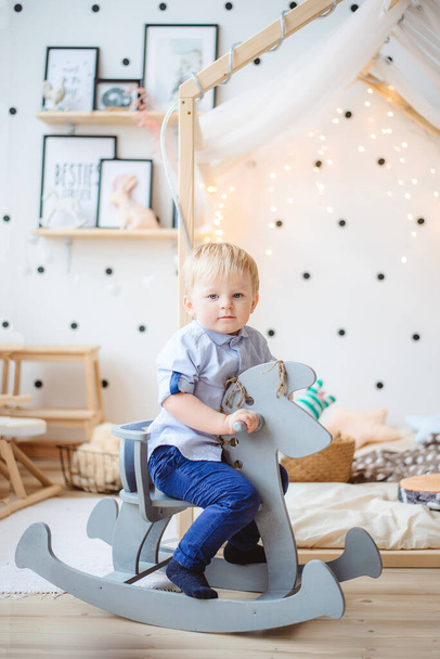 Ein kleiner Junge reitet auf einem Spielzeugpferd im Kinderzimmer. - Foto, Bild