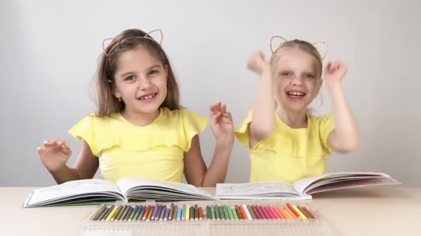 Grappige en grappige kinderen. Kinderen aan tafel dansen en creëren. Twee kinderen zitten aan een tafel en kleuren een kleurboek. - Video