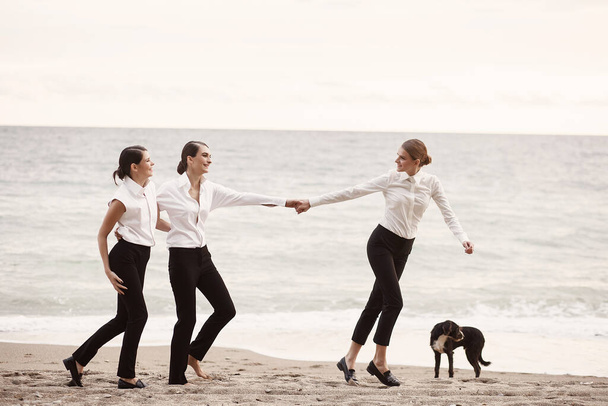 Een jong meisje trekt haar vriendinnen hand op een zandstrand, tegen de zee. - Foto, afbeelding