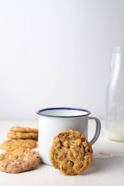 Primo piano della tazza bianca con biscotti con gocce di cioccolato e bottiglia di latte su sfondo bianco
 - Foto, immagini