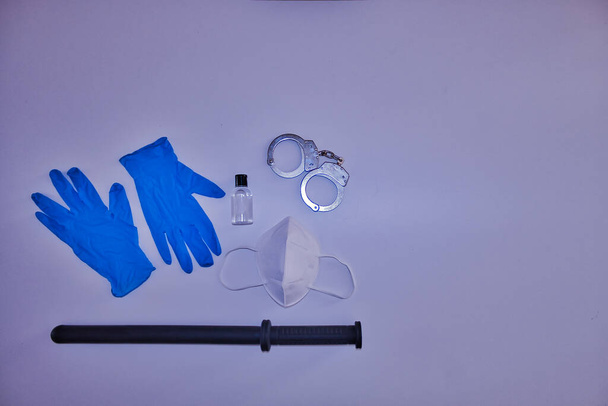 Policejní bezpečnostní vybavení od Covida19. Skládá se z modrých rukavic, hydroalkoholového gelu, pout, masky a obušku na bílém pozadí. - Fotografie, Obrázek