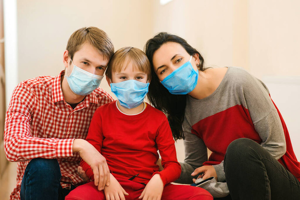 Güvenlik maskeli genç bir aile. Koronavirüsü önleme. Evde kal. Ev karantinası. Coronavirüs salgını. Ebeveynler ve çocuk cerrahi maske takıyor. Coronavirüs salgını. Yeni gerçek hayat. - Fotoğraf, Görsel