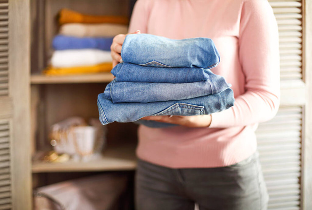 Jovem lojista segurando pilha de jeans sobre fundo claro em suas mãos. Fechar
 - Foto, Imagem
