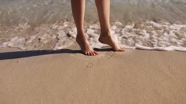 Ayaklar dalga tarafından yıkanır. Dalgalar kumsalda yuvarlanıyor. Kadın ayaklarını yıkıyor. Güneşin altında duruyor. Denizde dinlen.. - Video, Çekim