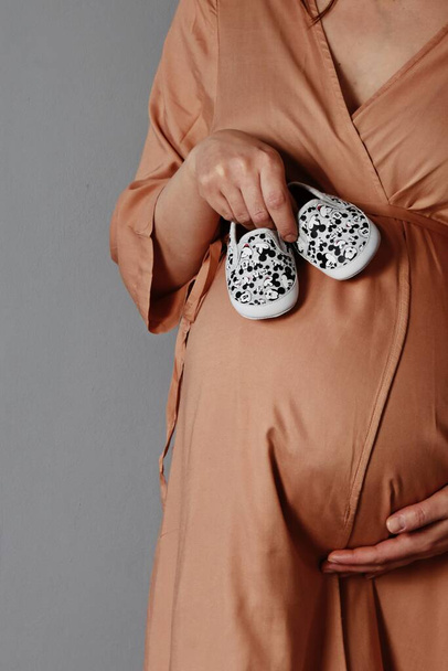 zwanger vrouw in beige jurk met kind schoenen, bijgesneden uitzicht   - Foto, afbeelding