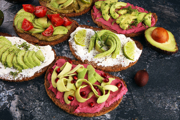 アボカドトースト。アボカドとトマトやビートルートなどのトッピングと健康的なライ麦の朝食サンドイッチのバリエーション - 写真・画像