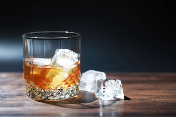 Стакан крепкого алкогольного напитка со льдом на деревянной барной стойке. Виски со льдом. Стекло с охлажденным напитком. - Фото, изображение