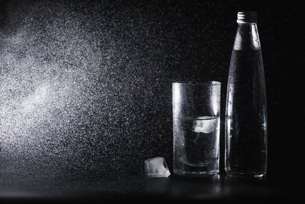 リビングルームのテーブルの上にボトルから精製された新鮮な飲料水を注ぐを閉じます。飲料水だ。ミネラルビタミン水。健康的でミネラルが豊富でさわやかな水. - 写真・画像