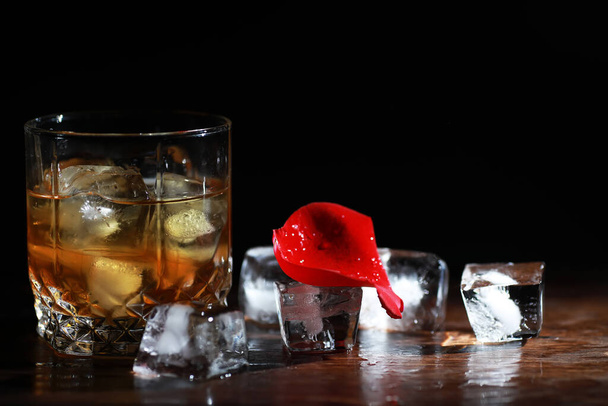 Ένα ποτήρι δυνατό αλκοολούχο ποτό με πάγο σε ξύλινο πάγκο μπαρ. Ουίσκι με παγάκια. Ποτήρι με παγωμένο ποτό. - Φωτογραφία, εικόνα