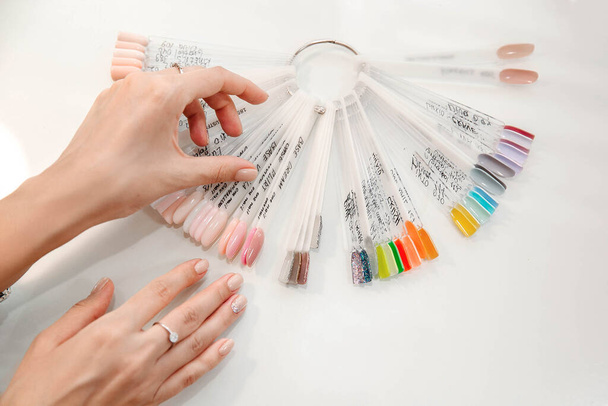 A woman is choosing color of  nail polish in a manicure salon, nude and pink colors, color palette - Fotó, kép