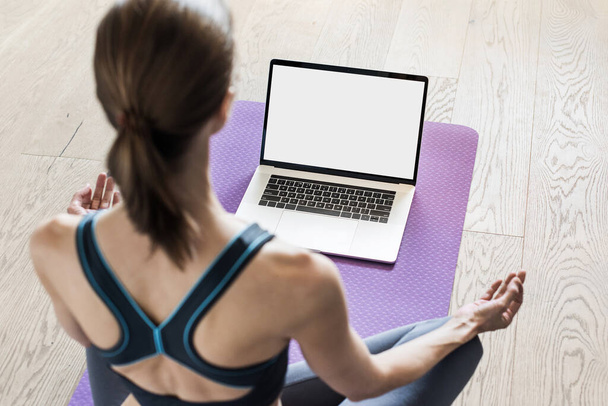 Young woman practicing yoga at home. Online video training. Girl doing exercises and meditate. Yoga, balance, meditation, relaxation, healthy lifestyle, online training concept. Blank empty monitor - Photo, image