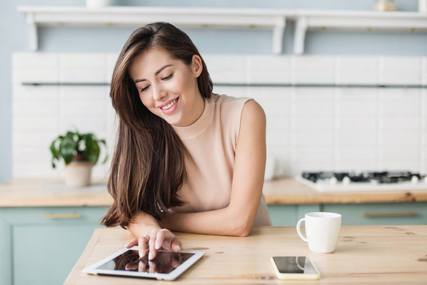 Cute smiling woman using digital tablet at home. Student girl reading or searching recipe. Online shopping, work from home, freelance, online learning, studying, lockdown concept. Distance education - Fotó, kép