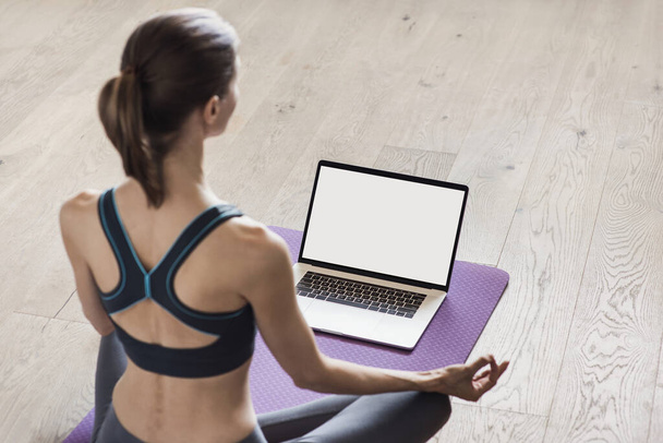 Young woman practicing yoga at home. Online video training. Girl doing exercises and meditate. Yoga, balance, meditation, relaxation, healthy lifestyle, online training concept. Blank empty monitor - Foto, imagen