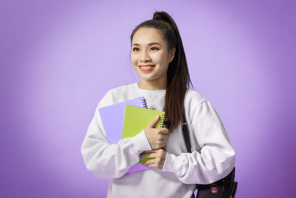 Portrait of beautiful young asian holding notebooks isolated on the violet background - Photo, Image