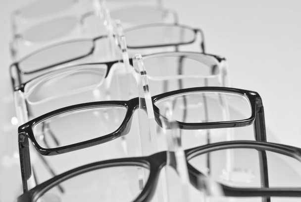 Many glasses on a white background. Glasses are stacked in a row on a transparent shop window. Glass stand on gray table. Sale and exhibition of optics. - 写真・画像