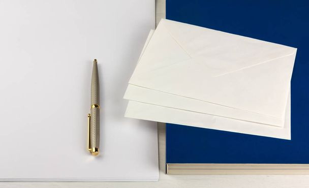 Книга, три конверта, элегантная ручка и маленькая груда белых бумажных простыней на деревянном столе
 - Фото, изображение