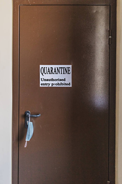 Железная дверь в больничную палату с предупреждающей надписью QUARANTINE. Несанкционированный вход запрещен. Защитная маска весит на дверной ручке. Коронавирус Пандемический, Ковид-19
 - Фото, изображение