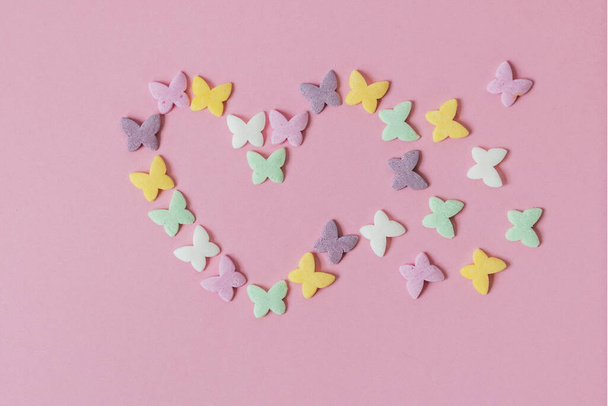 Pâtisserie multicolore saupoudrer-papillons sont disposés sous la forme d'un cœur en décomposition sur un fond rose. Décoration de produits de confiserie
 - Photo, image