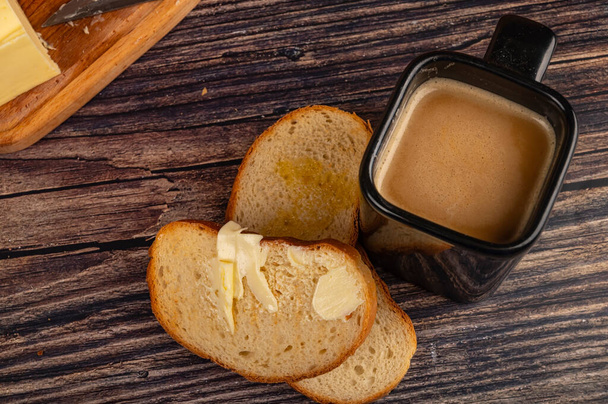 Čerstvý pšeničný toust s máslem, keramický hrnek s kávou a mlékem a kus másla v dřevěné plechovce na dřevěném pozadí. Zavřít - Fotografie, Obrázek