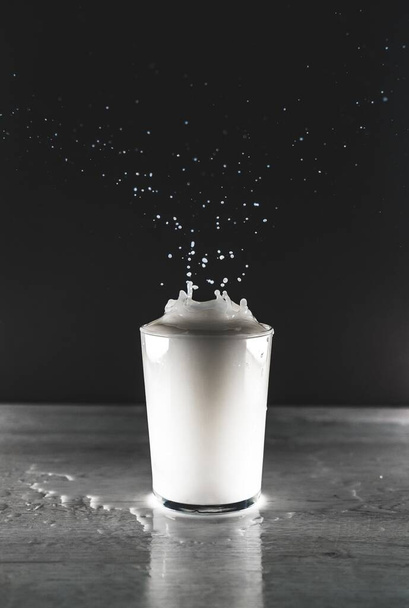 A grayscale vertical view of a white liquid splash in a glass cup - Foto, imagen