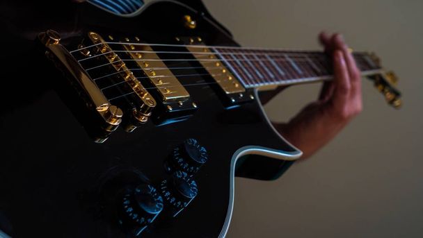 A low angle closeup of a person playing a black electric guitar under the lights in a room - Valokuva, kuva