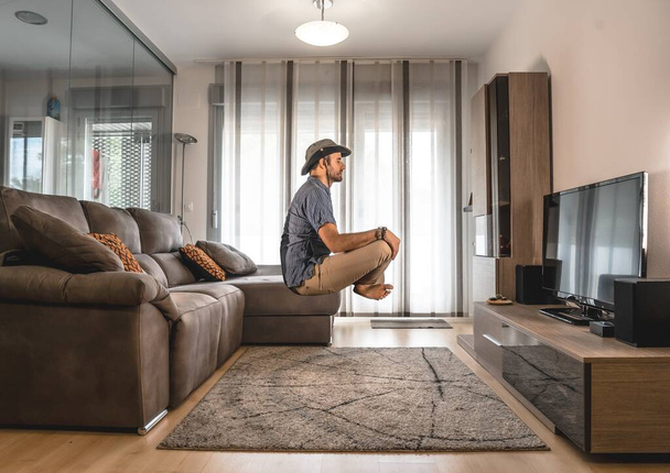 A male meditating and floating in the air in front of the TV in the living room - Fotó, kép