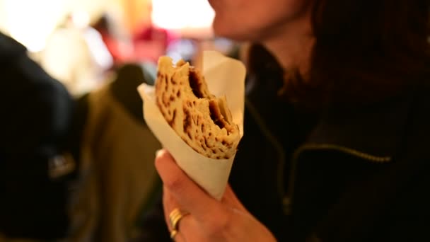 Ραβέννα, Ιταλία - Δεκέμβριος 2019: Μια δυσδιάκριτη λευκή γυναίκα τρώει μια πιαδίνα Romagna, μια ιταλική σπεσιαλιτέ που εκτιμάται ιδιαίτερα από τους τουρίστες. Μπορείτε να δείτε τη νόστιμη γέμιση ζαμπόν και τυριού. - Πλάνα, βίντεο