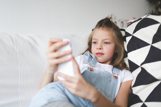 young girl with smartphone on couch is doing video call during the corona crisis - Fotografie, Obrázek