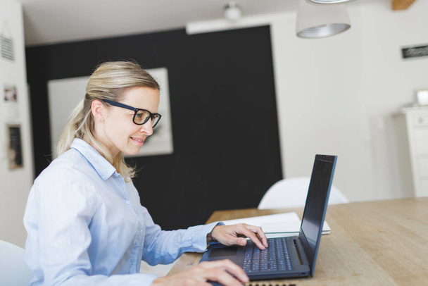 pretty young businesswoman with blue shirt and glasses working in home office - Foto, imagen