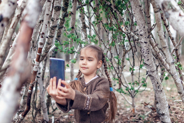 Junges Mädchen plaudert auf dem Handy im erbauten Holzhäuschen im wilden Birkenwald während ihres geselligen Spaziergangs in der Ruhezeit, Spazierengehen an der frischen Luft, aktiver Lebensstil im Freien - Foto, Bild