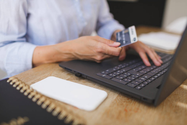 обрезанный снимок деловой женщины, делающей покупки дома со своим ноутбуком и кредиткой на кухонном столе
 - Фото, изображение