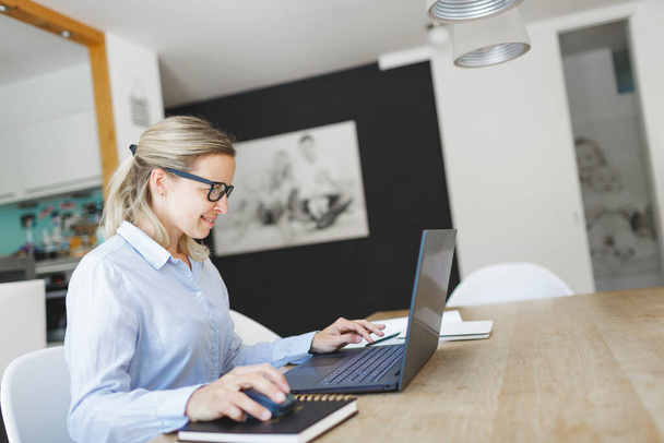 pretty young businesswoman with blue shirt and glasses working in home office - Foto, afbeelding