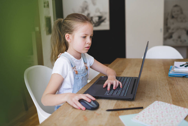 コロナ危機の家庭教育中にノートパソコンで働いていた女の子が - 写真・画像