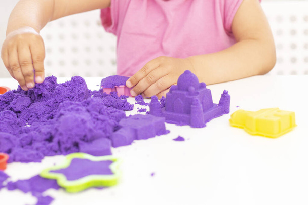 Childrens hands plays kinetic sand in quarantine. purple sand on a white table. coronavirus pandemic - Foto, Bild