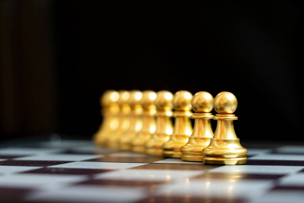 Peão de ouro peça de xadrez stand com outro como a linha no fundo preto
 - Foto, Imagem