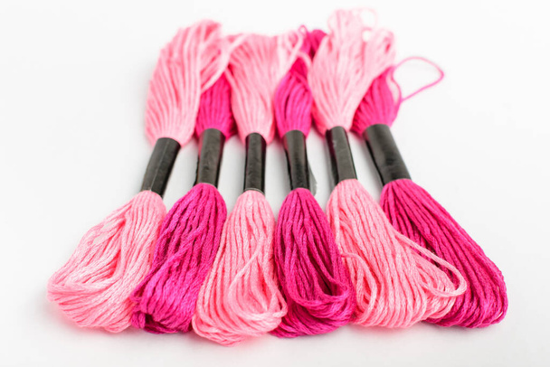 Seis hilos de coser rosados vivos mezclados para bordar aislados en una mesa blanca, vista superior o plano de materiales textiles
 - Foto, imagen