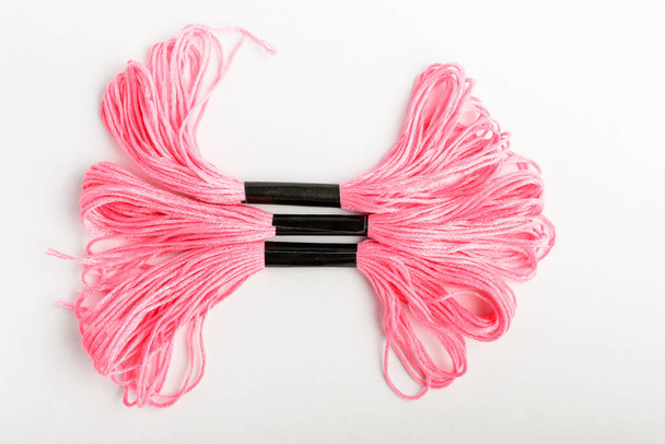 Tre vivaci fili da cucito rosa per il ricamo isolati su una tavola bianca, vista dall'alto o posa piatta di materie tessili
 - Foto, immagini