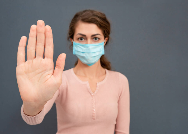 Žena v lékařské masce na tváři s nápisem stop coronavirus s rukama na šedém pozadí. Lidé chrání svůj život před viry a infekcemi. Kavkazská dívka Zůstaň doma, koronový virus. - Fotografie, Obrázek