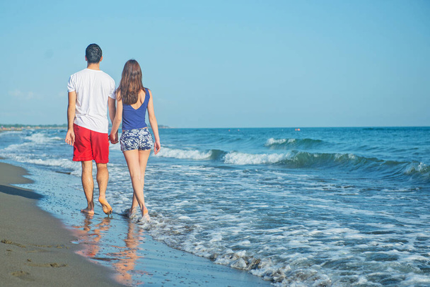 rear view of couple walking by sea shore at daytime - Foto, afbeelding