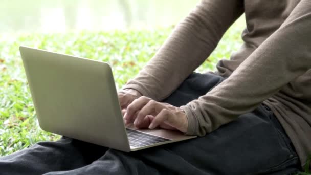 Zárja be a két kéz a férfi segítségével notebook és ujjak érintse meg a billentyűzet számítógép szabadtéri zöld park. - Felvétel, videó