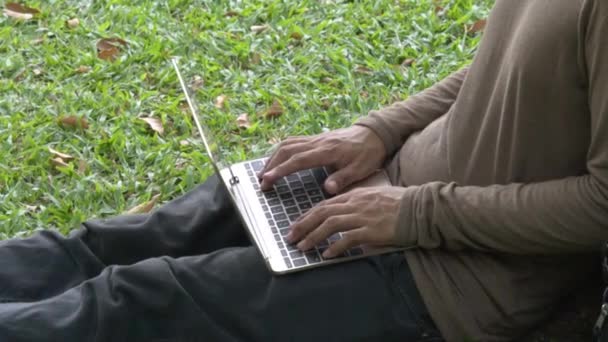 Cierre dos manos del hombre usando el portátil y los dedos tocan en la computadora del teclado en el parque verde al aire libre. - Metraje, vídeo