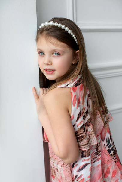 A beautiful blonde little girl in a dress turned around and looks at the camera. Portrait of beautiful child girl whith blue eyes. - Foto, Imagem