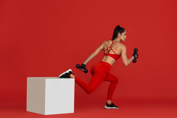 Beautiful young female athlete practicing on red studio background, monochrome portrait - Zdjęcie, obraz