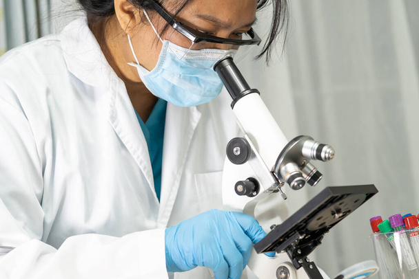 Cientista asiático bioquímico ou microbiologista trabalhando pesquisa com um microscópio em laboratório. Para proteger o surto Coronavirus Covid19, bactérias e germes. - Foto, Imagem