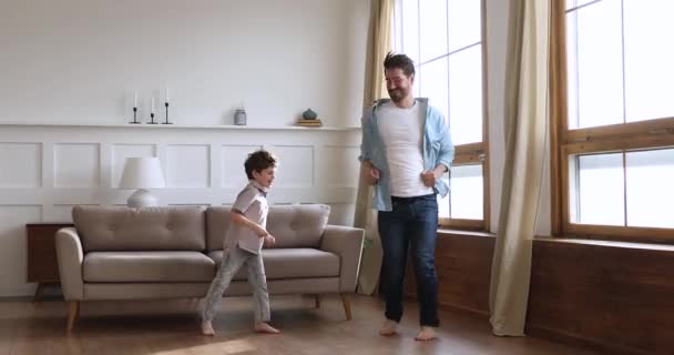 Νεαρός πατέρας χορεύει σε θερμαινόμενο ξύλινο πάτωμα με μικρό γιο. - Πλάνα, βίντεο