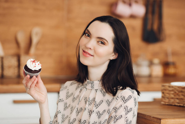 Knappe jonge vrouw gemaakt marshmallows en eet het in haar grote heldere keuken met plezier - Foto, afbeelding