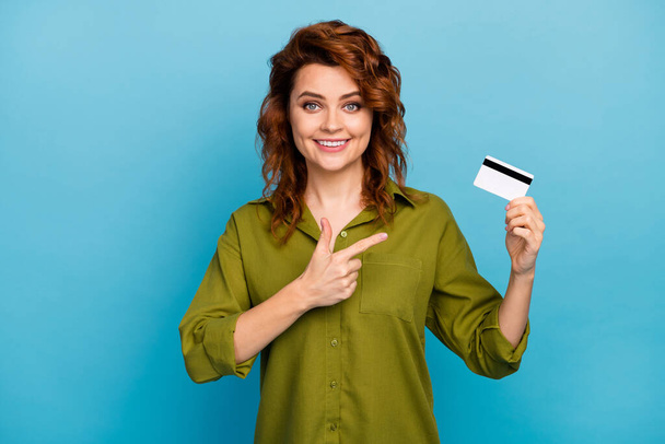 Portrait of positive confident cool woman hold credit card suggest select banking easy paying service point index finger wear good look green shirt isolated over blue color background - Foto, Imagem