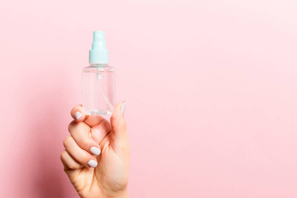 Close-up van cosmetica spray in vrouwelijke hand op roze achtergrond met kopieerruimte. - Foto, afbeelding