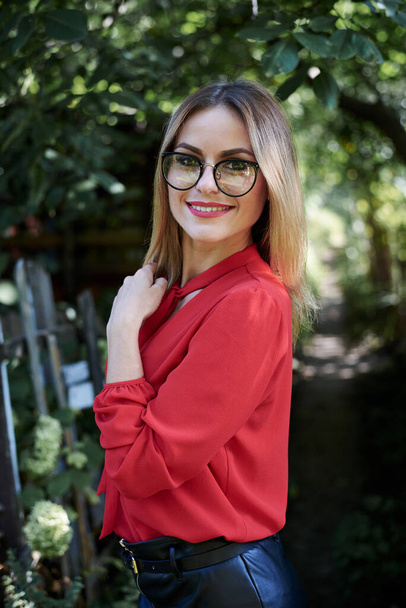 Close-up portrait of attractive young woman with short blond hair, wearing eyeglasses, smiling in the summer garden, Happy female student, posing in the park. Sunny day in campus. - Фото, зображення
